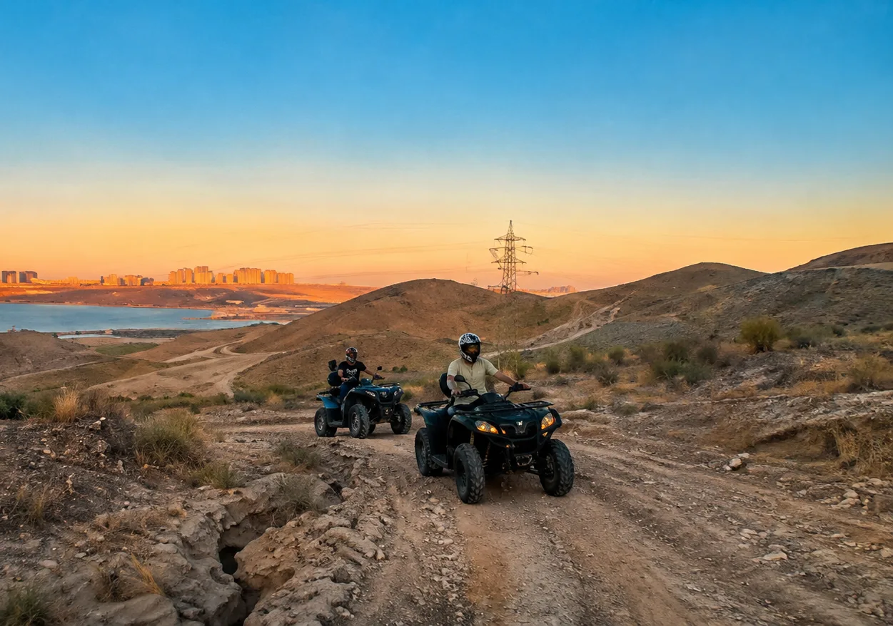 Two quad bike riders on an Absheron hill trail at sunset, Baku skyline across the bay
