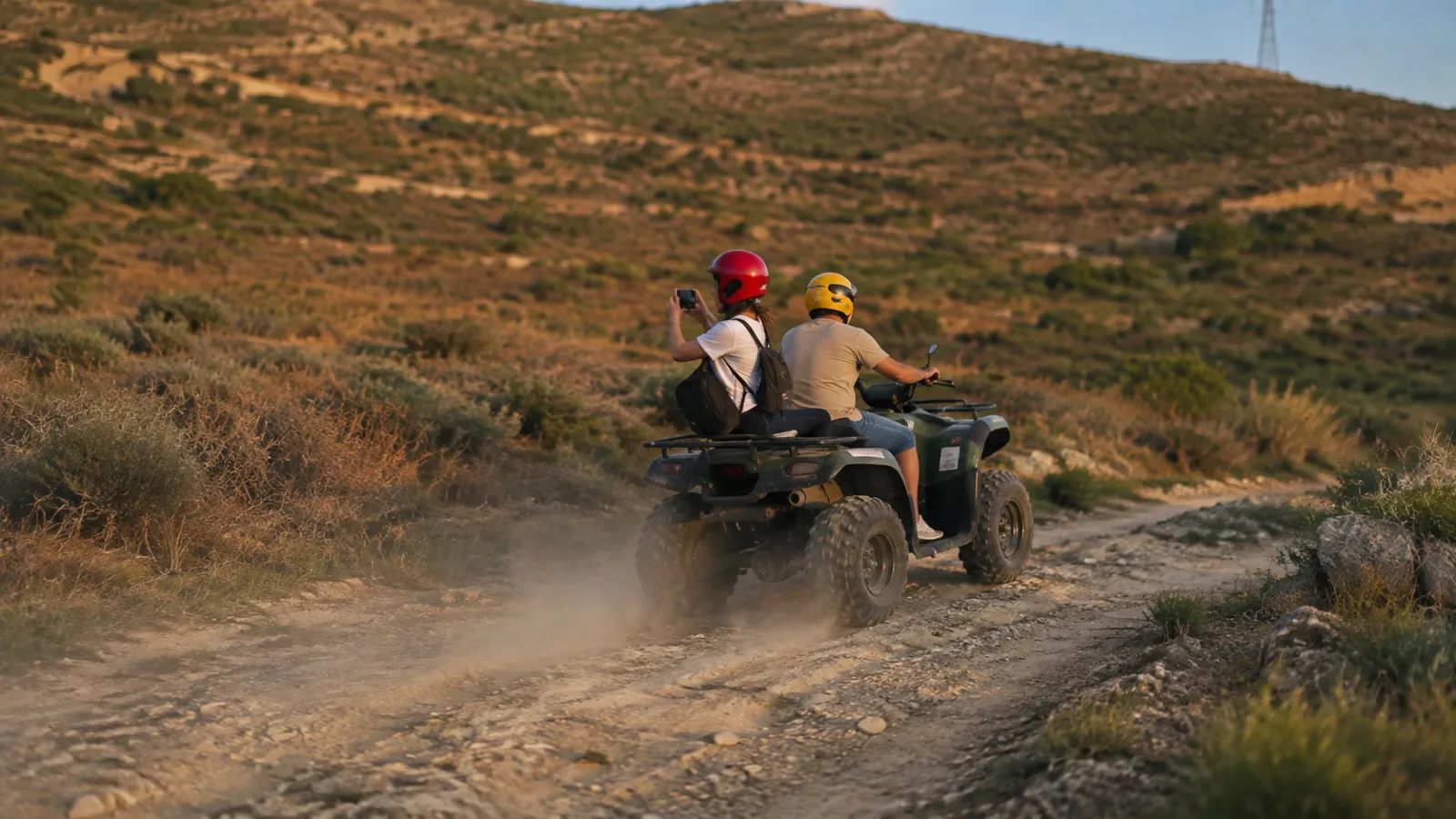 Couple riding two-up on a quad bike on a dusty Absheron trail at golden hour